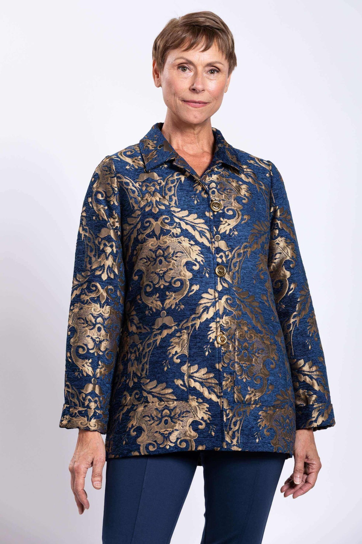 Front view of woman wearing a blue and gold jacquard short coat with brass buttons