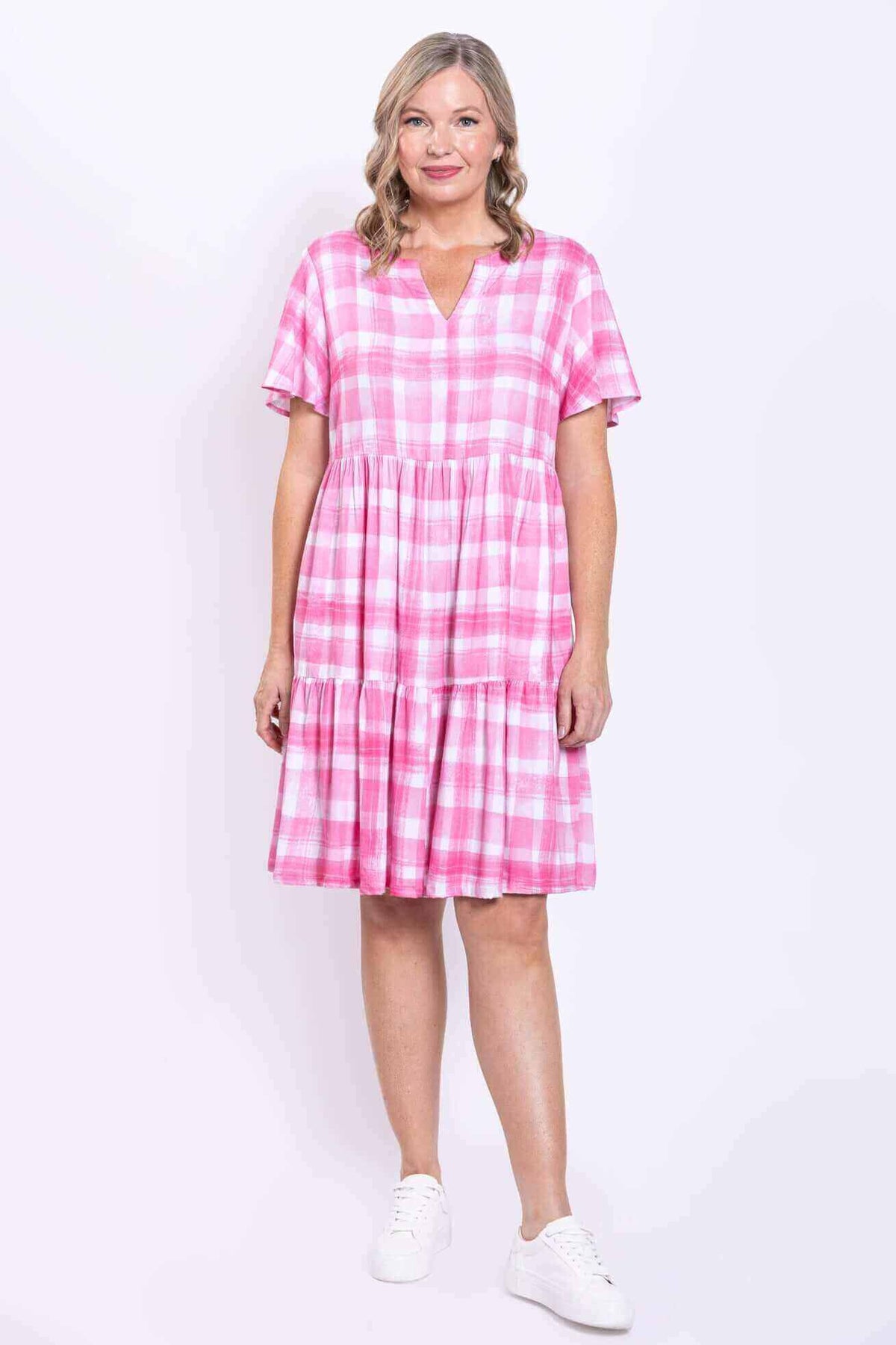 Front view of woman wearing a pink check short sleeve tiered dress with V notch neckline