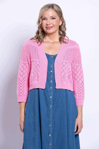Front view of woman wearing pink cropped pointelle knit cardigan over blue dress