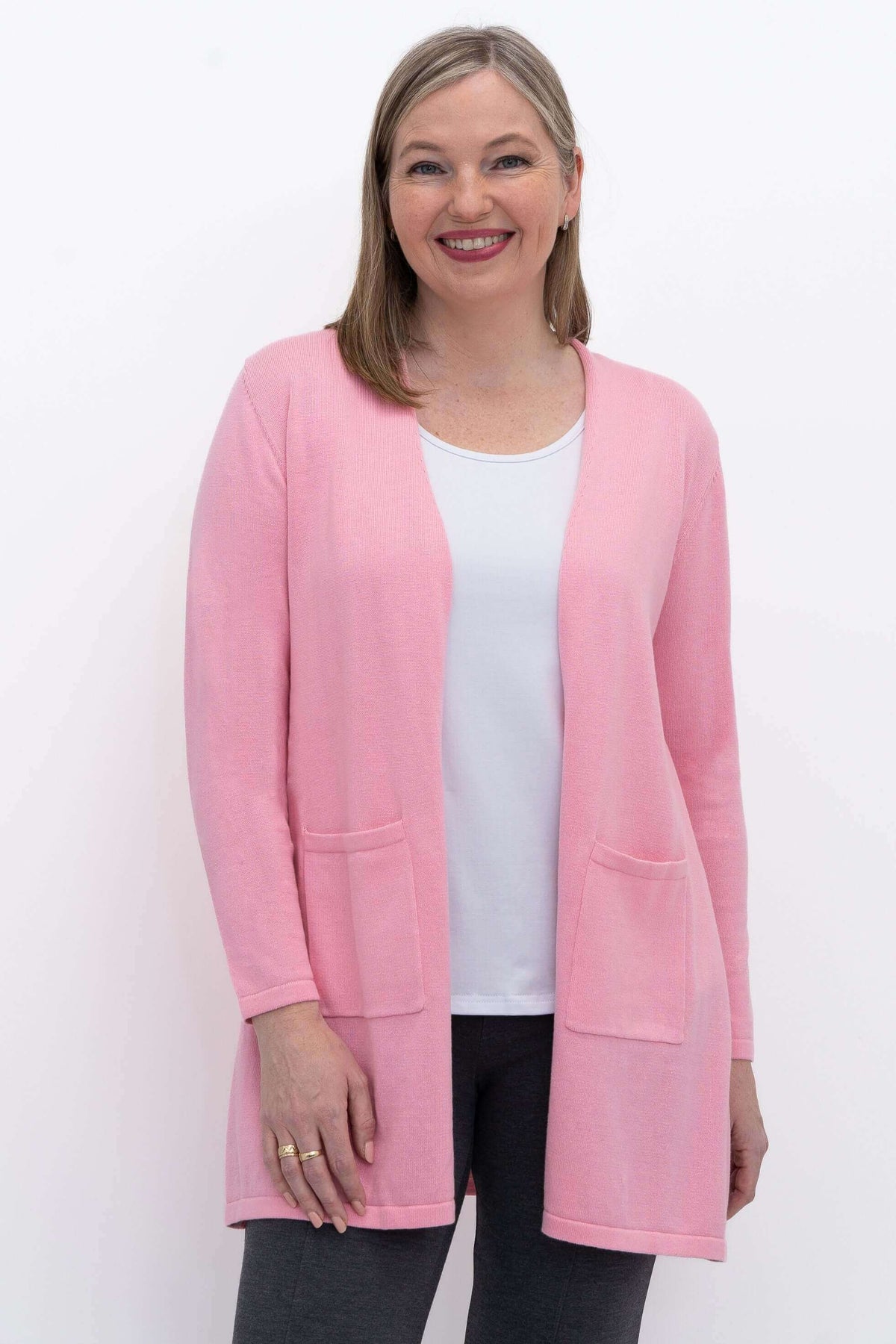 Front view of a woman wearing a pink open-front cotton cardigan with patch pockets