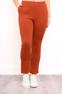 Front view of a woman wearing rust orange bamboo slim fit pants with an elastic waistband and ankle slits.
