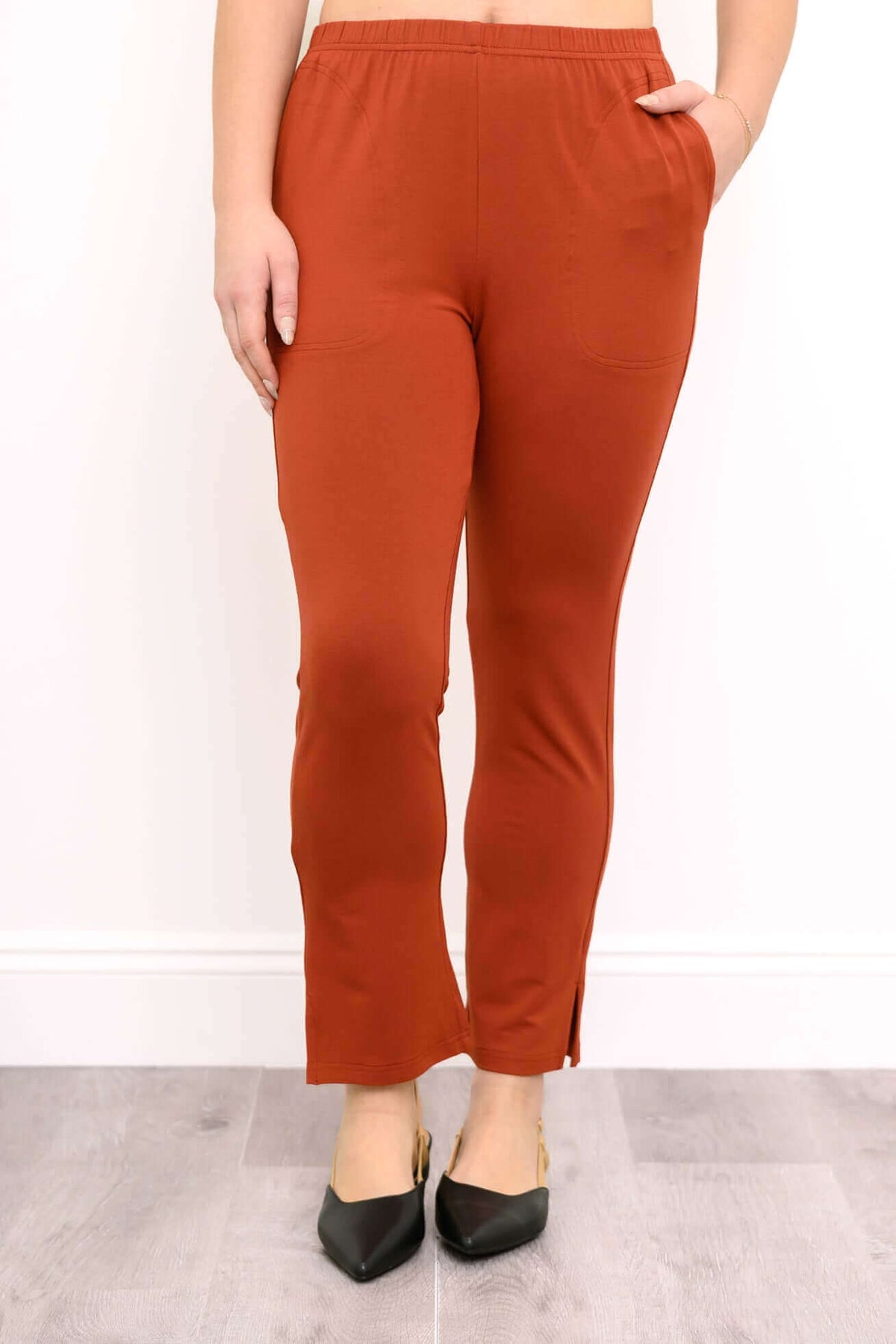 Front view of a woman wearing rust copper bamboo slim trousers elevated with stylish black pointed pumps.