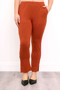 Front view of a woman wearing rust copper bamboo slim trousers elevated with stylish black pointed pumps.