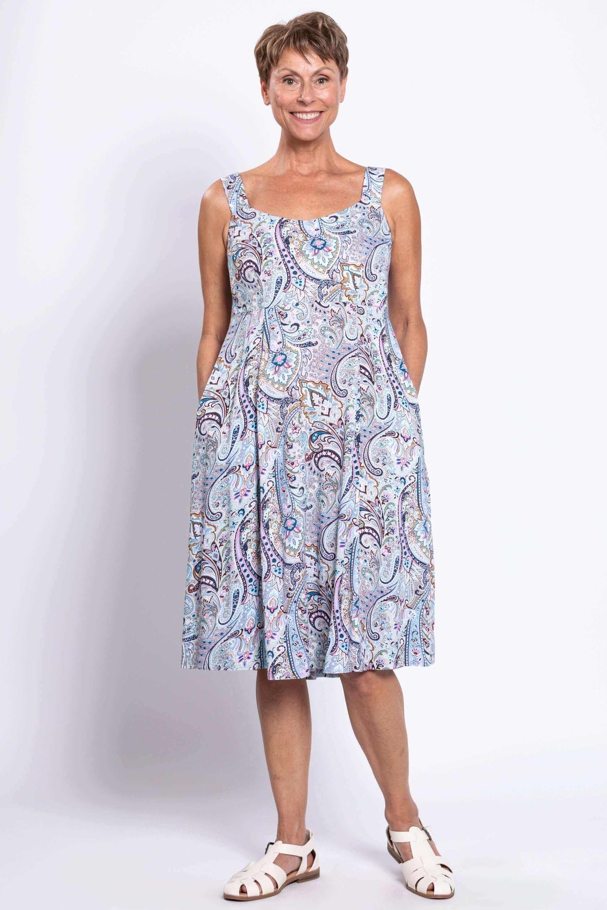 Front view of a woman in a scoop neck sleeveless paisley dress with pockets, smiling