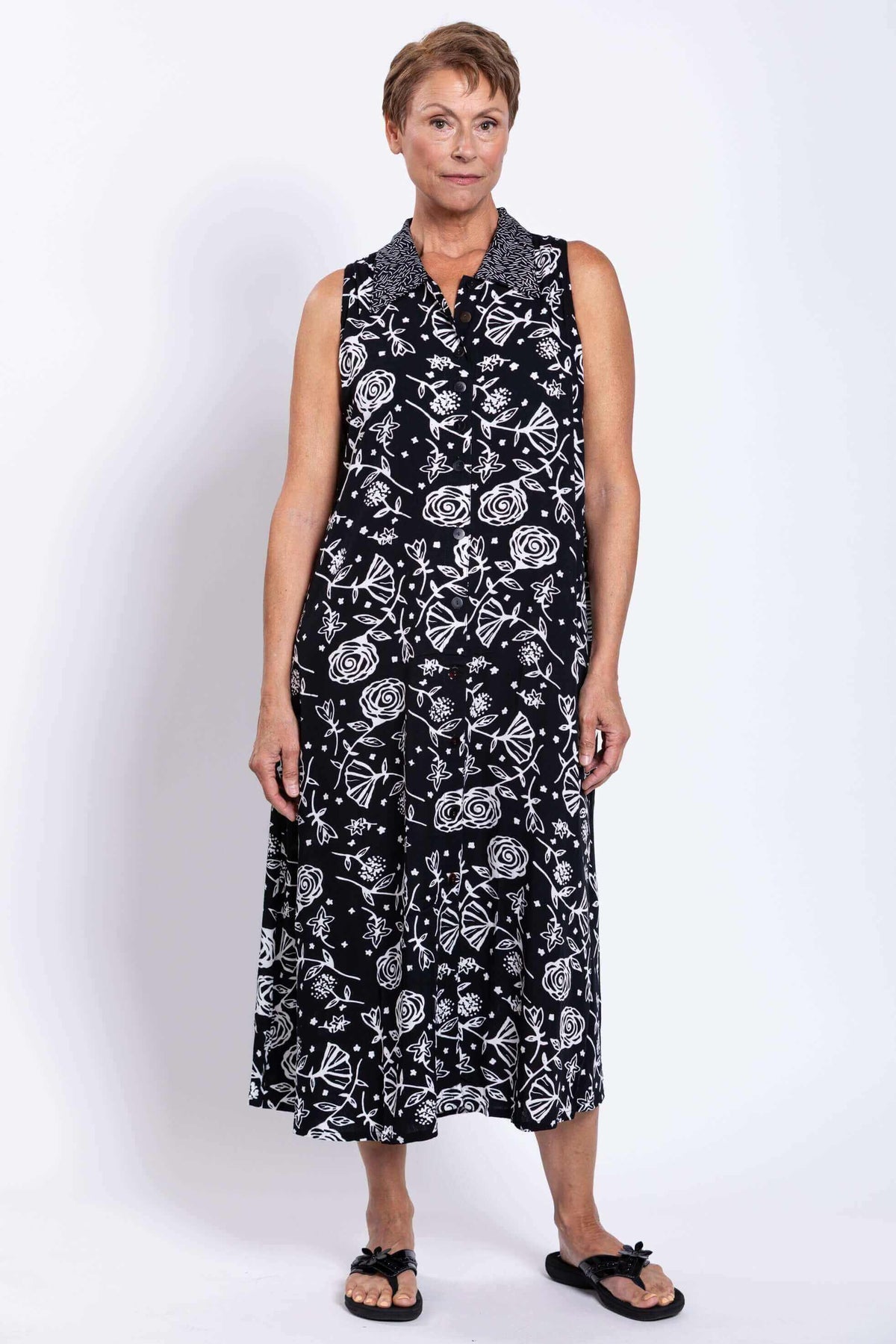 Front view of woman wearing sleeveless black A-line dress with white floral print