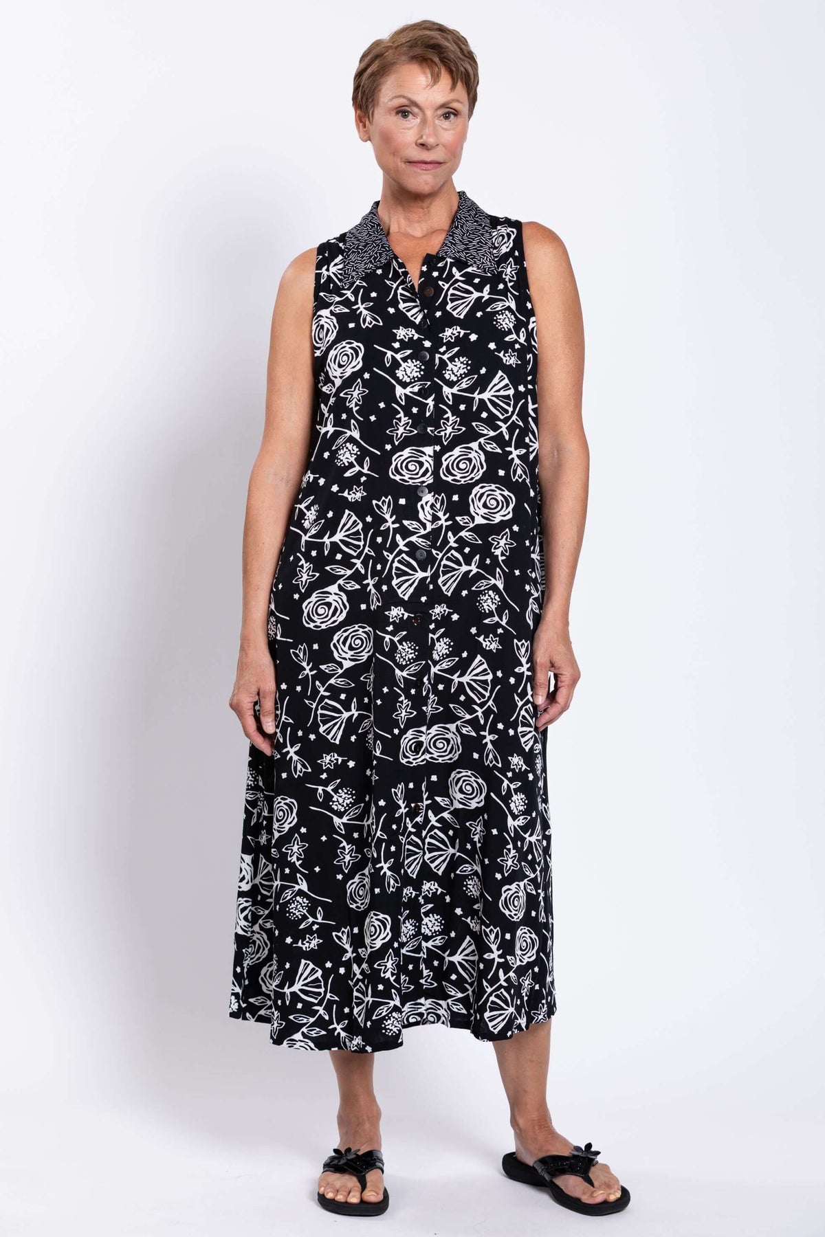 Front view of a woman wearing a sleeveless black A-line dress with white floral patterns