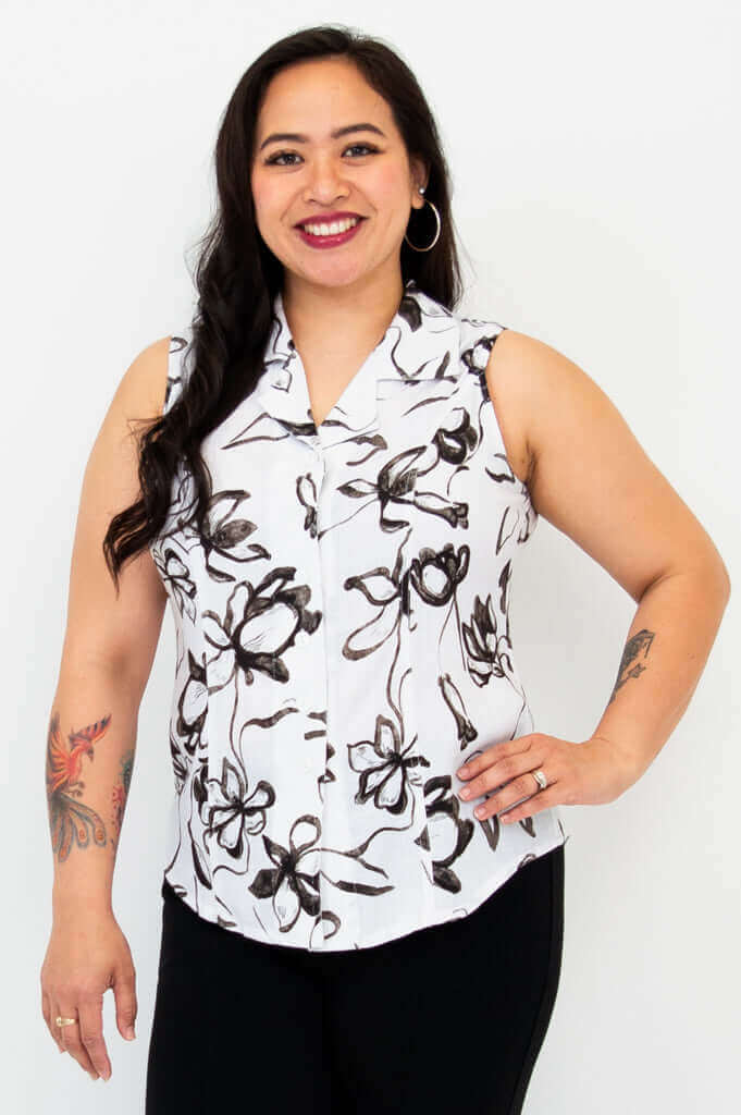Woman wearing a sleeveless white shirt with black floral print and black pants, front view