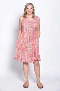 Woman wearing a sleeveless coral floral print dress with pockets, front view