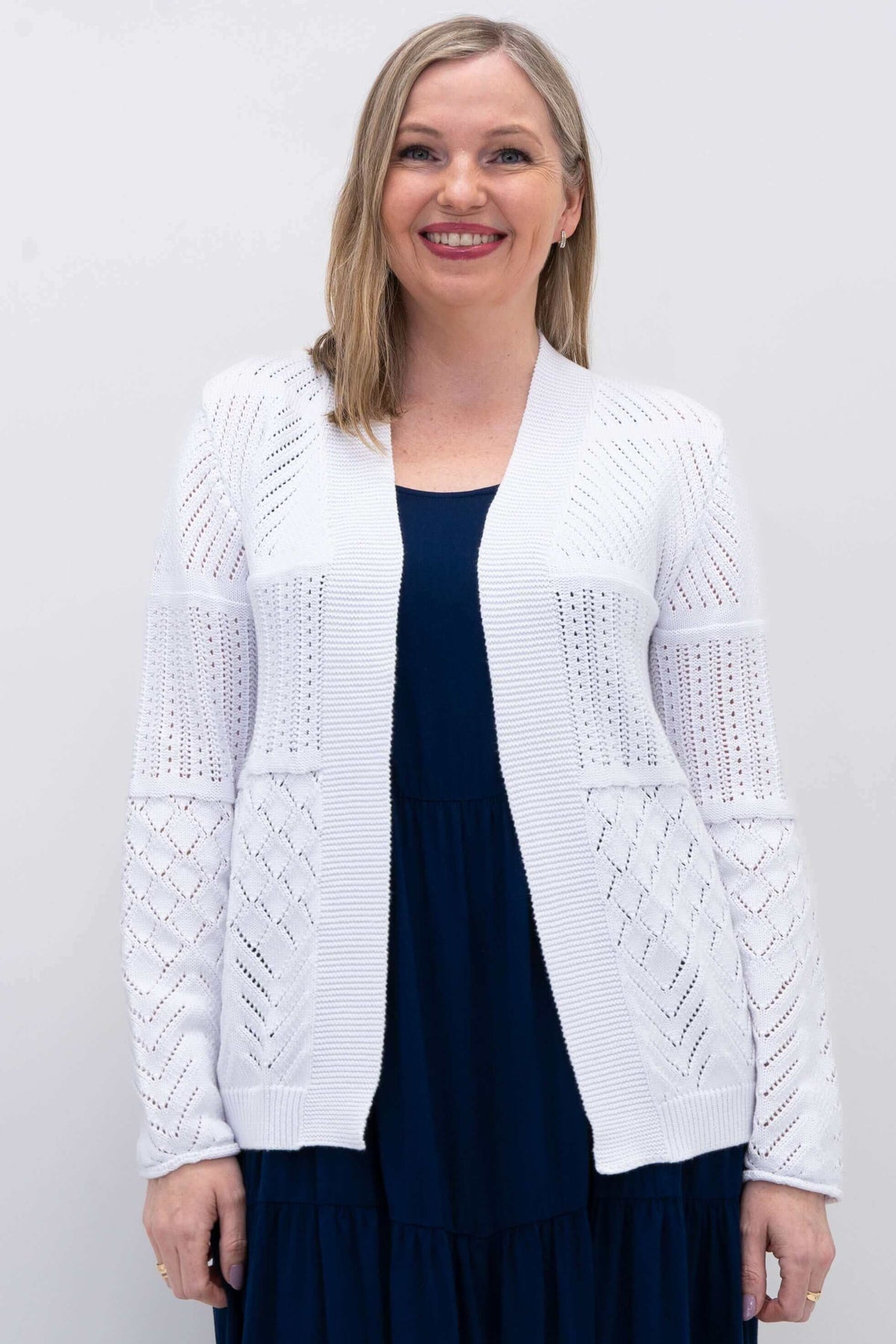 Front view of a woman wearing a white pointelle knit open cardigan over a navy dress