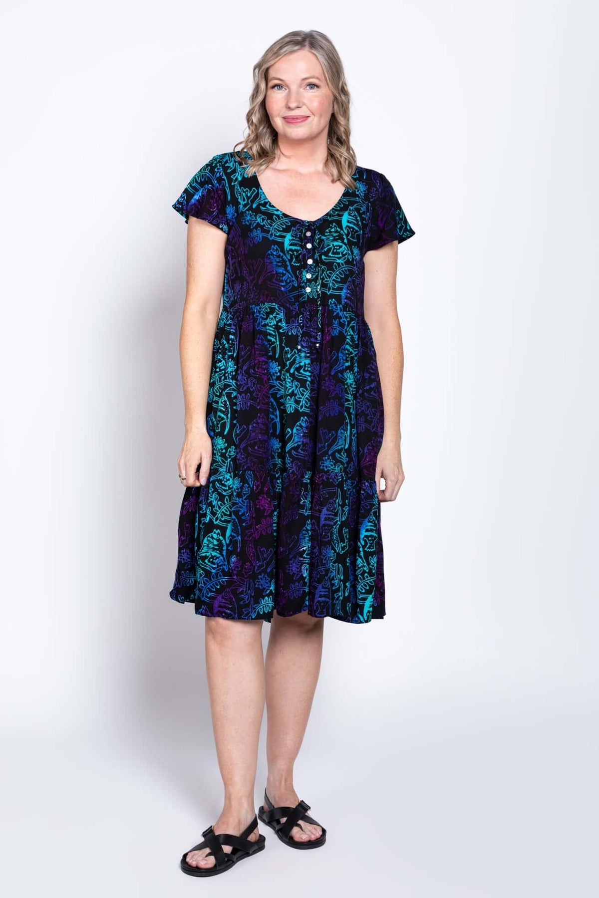Woman wearing a short sleeve, tiered black dress with blue and purple botanical print, front view