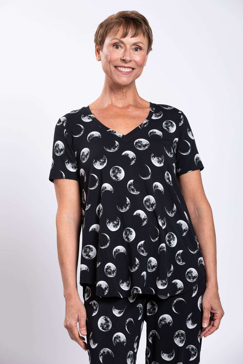 Woman wearing a black V-neck short sleeve top and pants with a moon phase print, front view