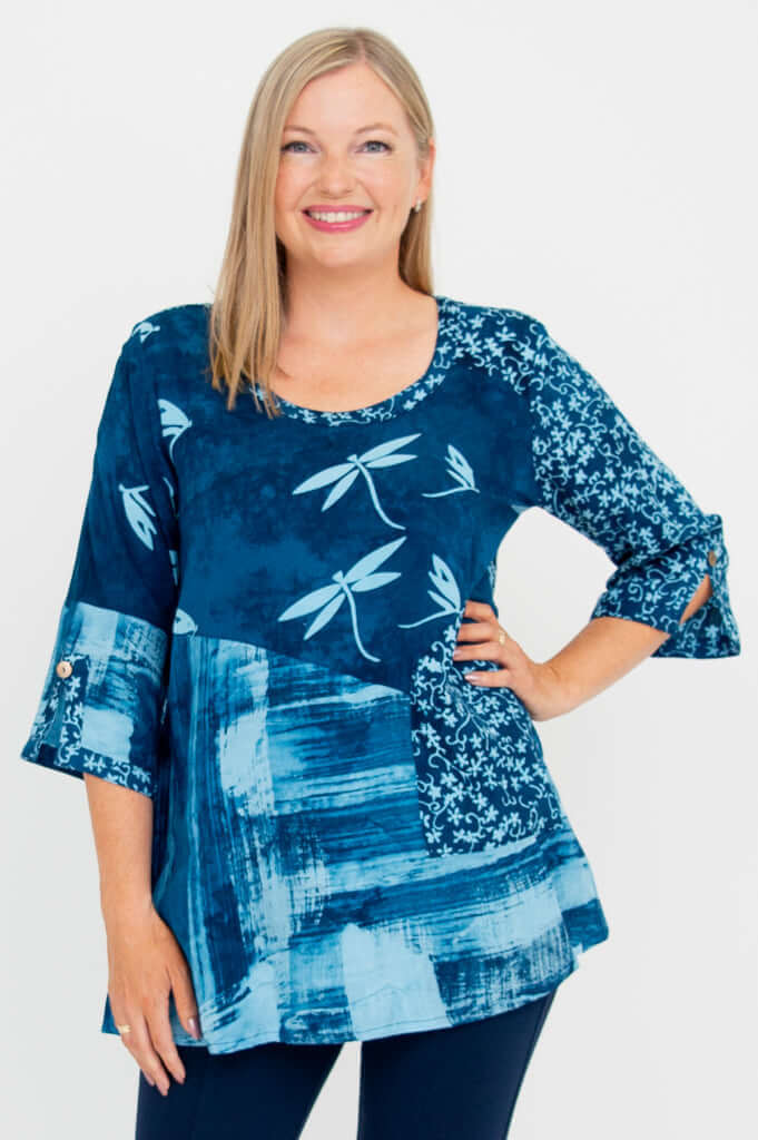 Woman wearing a blue flowy blouse with dragonfly and abstract patterns, front view