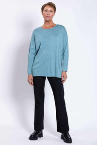 Woman in blue relaxed fit sweater and black pants, hands by side, facing front