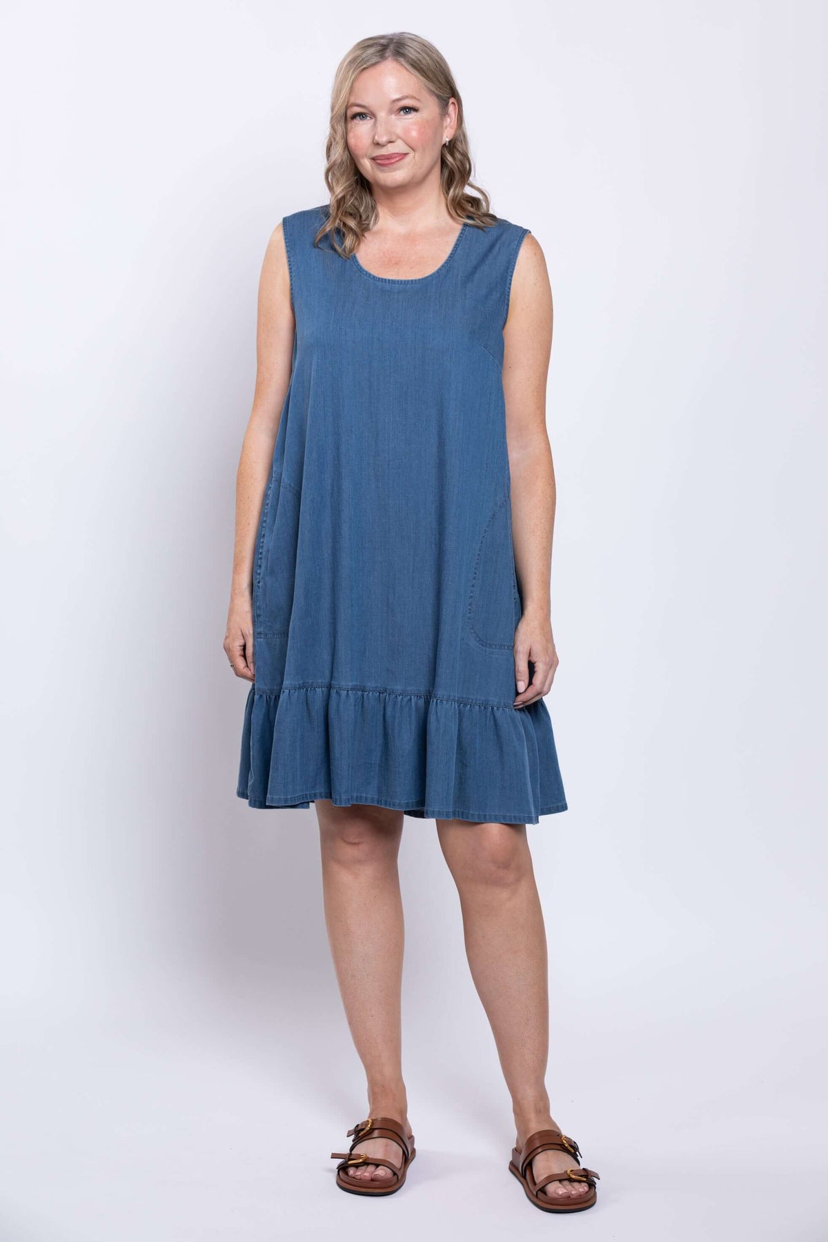 Front view of a woman in a blue sleeveless dress with round neck and ruffle hem