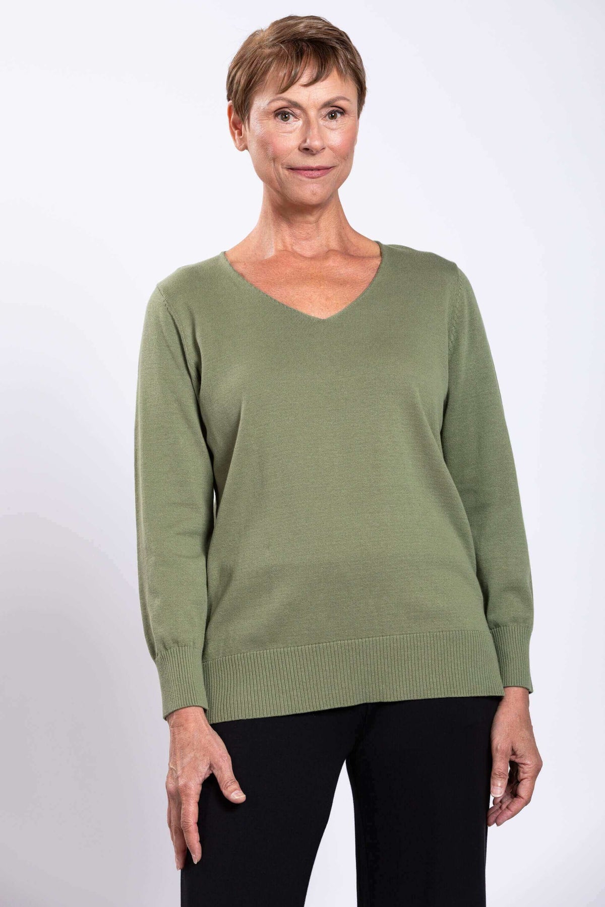 Front view of a woman wearing a green V-neck cotton sweater with black pants