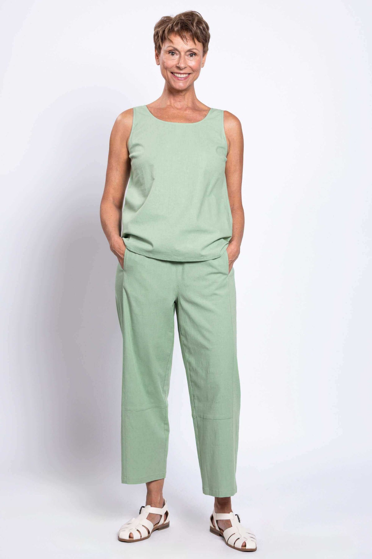 Woman wearing a sleeveless green linen top and cropped boardwalk pants, front view with hands in pockets