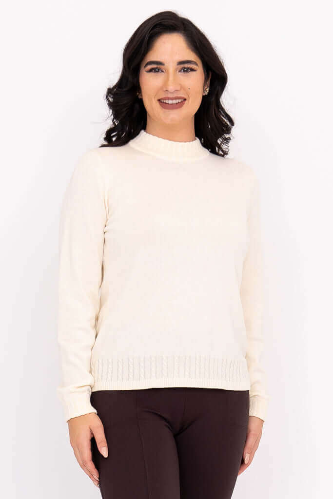 Full length view of a woman wearing a cream cotton mock neck sweater styled with dark brown pants.
