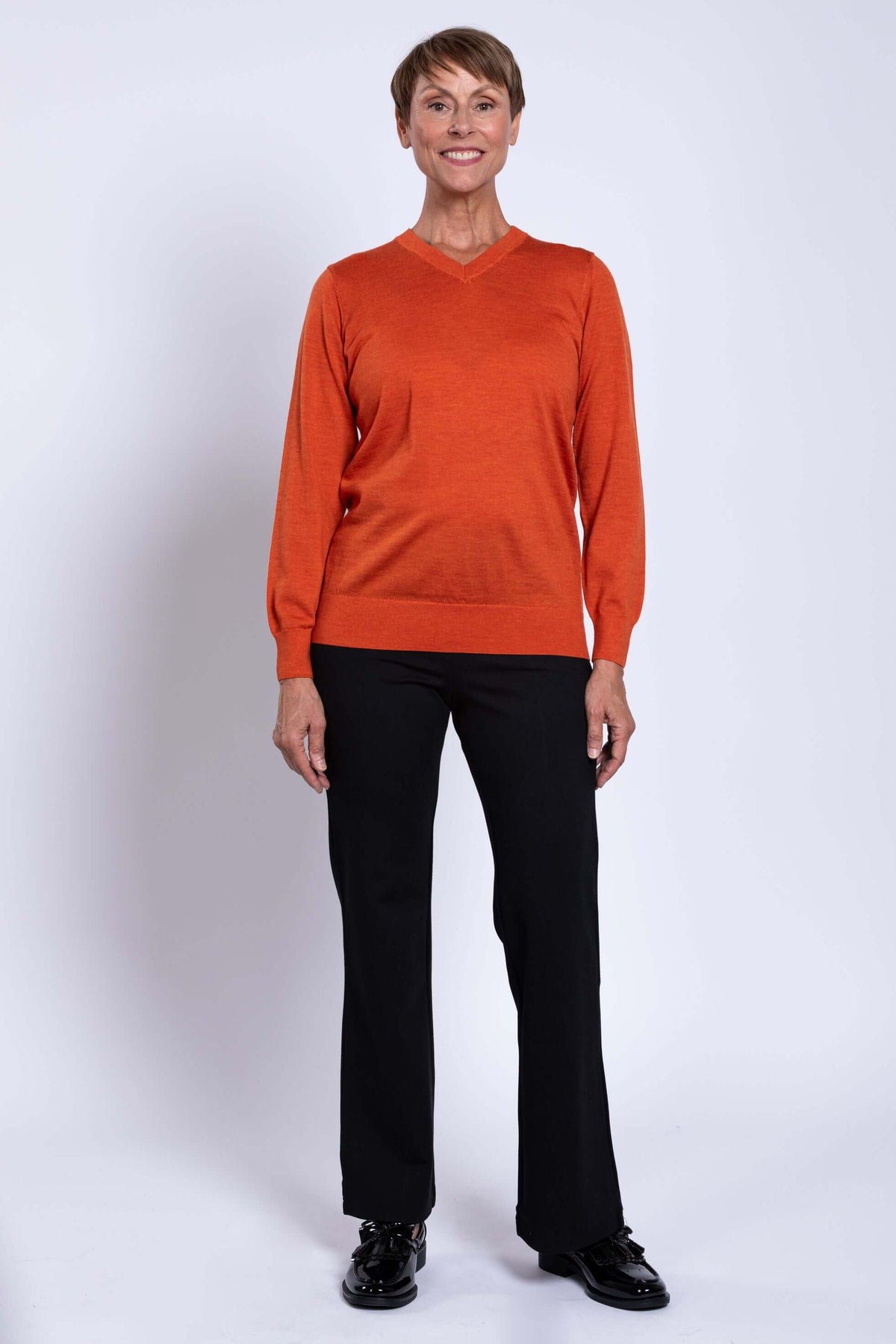 Front view of woman in orange V-neck sweater and black trousers