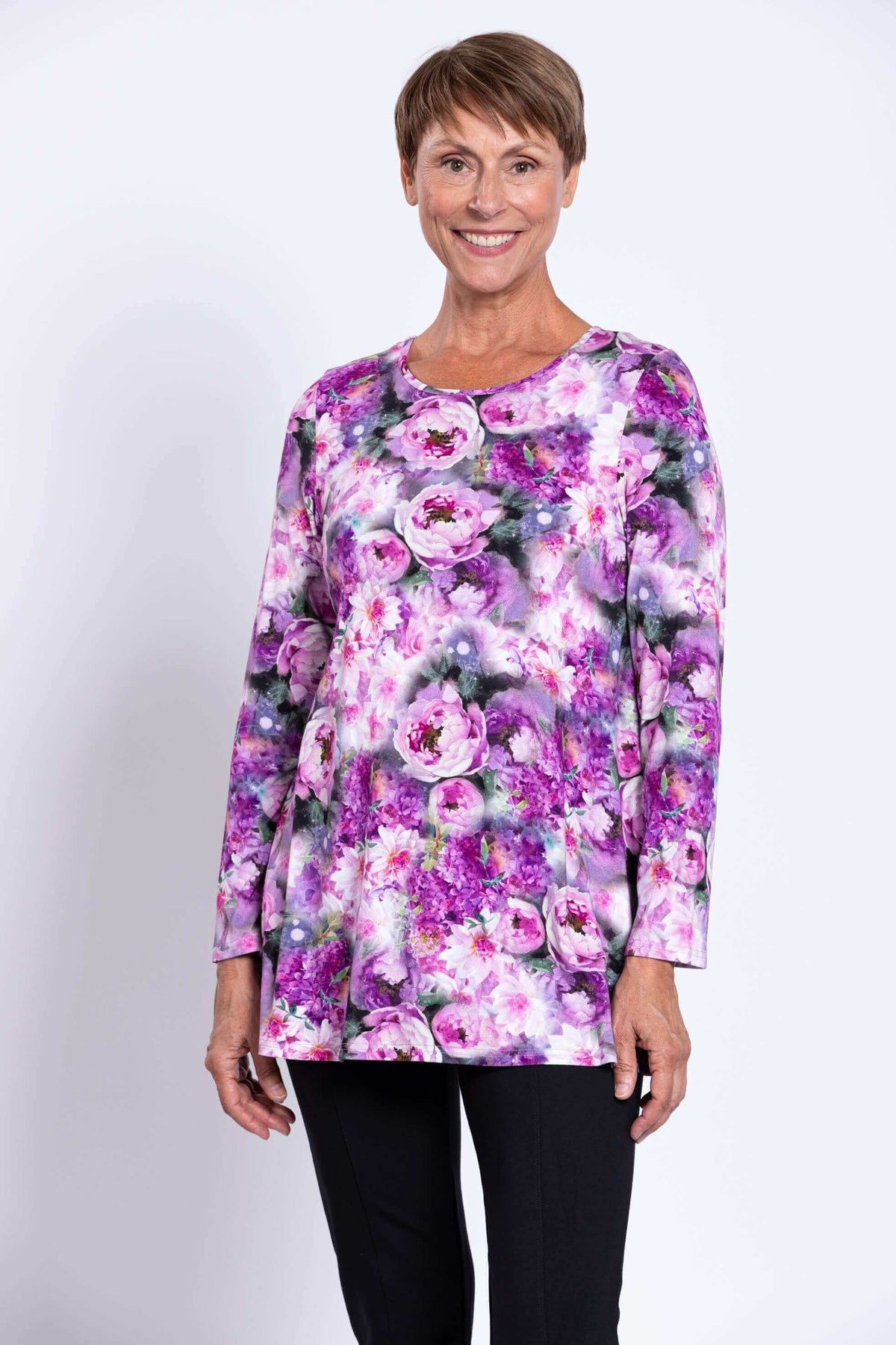 Front view of a woman wearing a long sleeve floral tunic in purple and pink