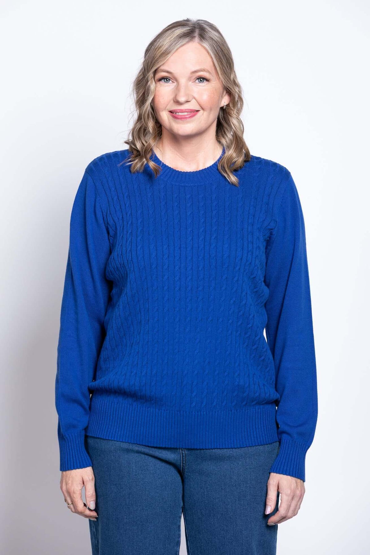 Close up front view of a woman wearing a royal blue cotton cable knit crewneck sweater.
