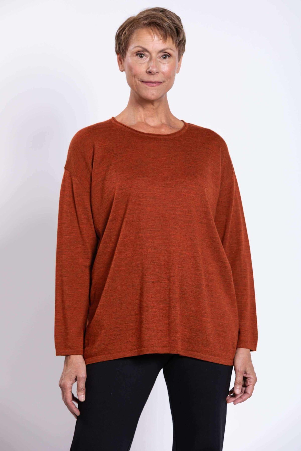 Front view of woman wearing rust Merino wool sweater with long sleeves and relaxed fit