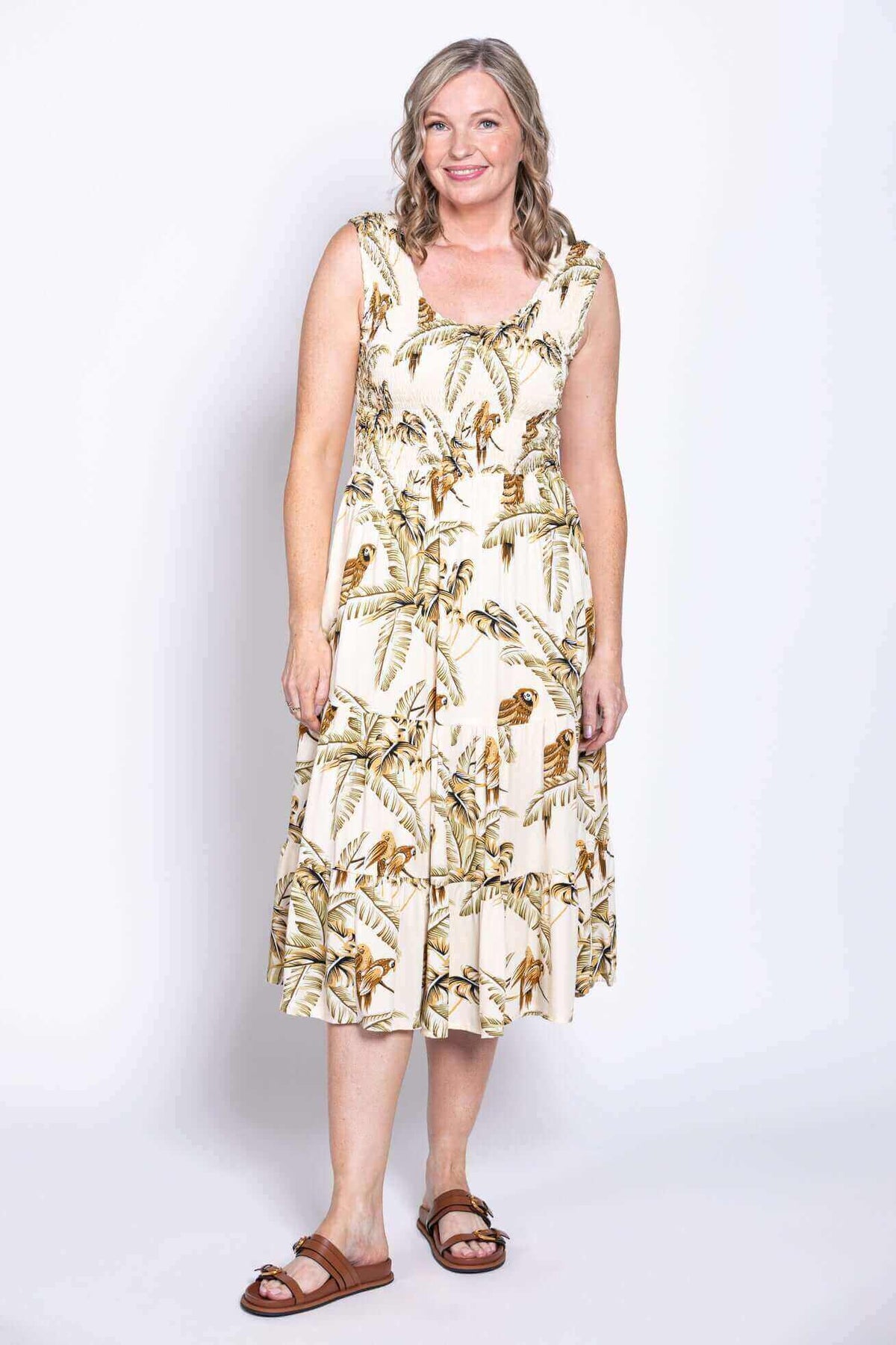 Woman wearing a sleeveless midi dress with tropical palm and bird print, standing front facing