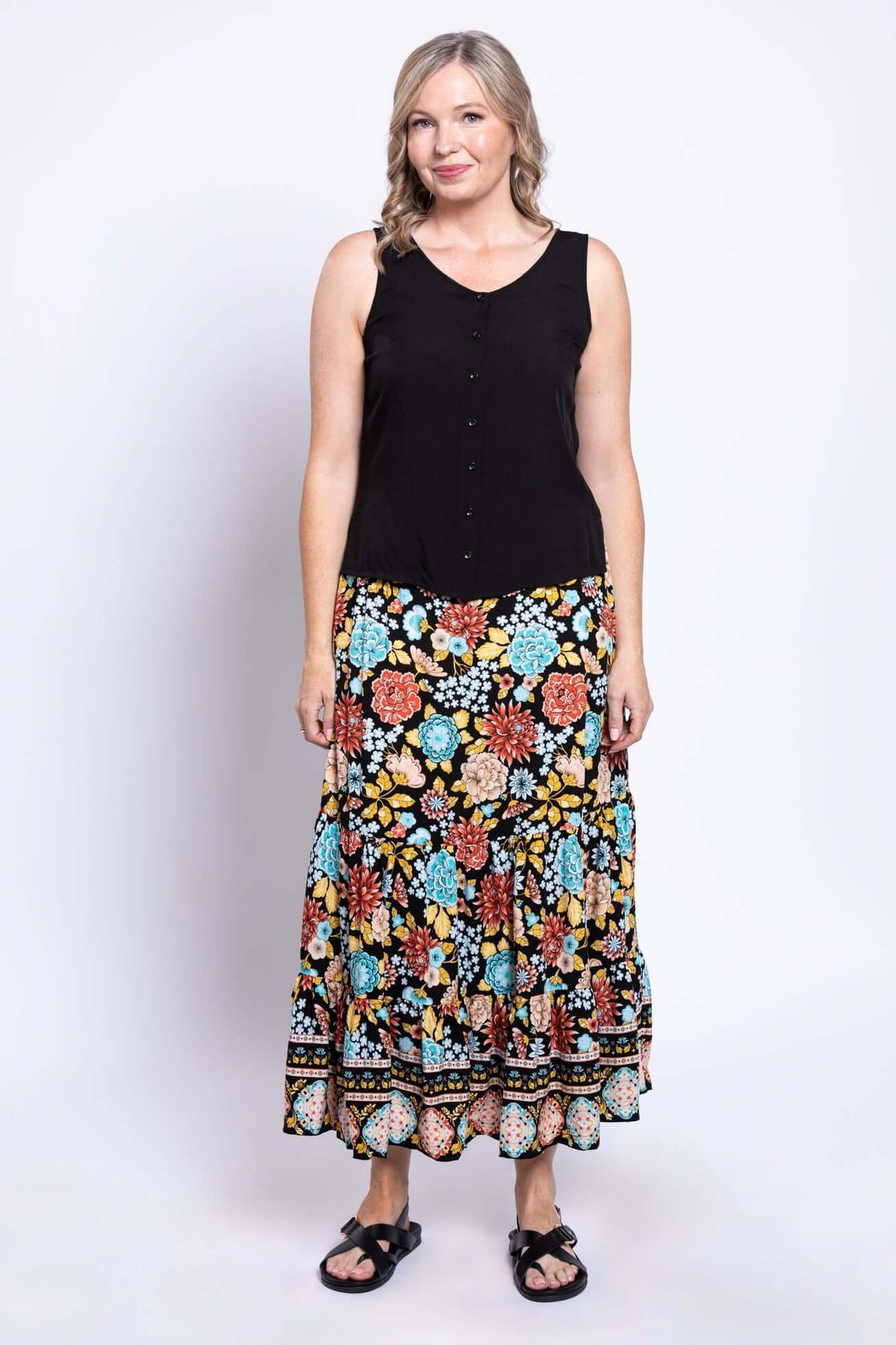 Woman standing front-facing in a vibrant floral maxi skirt and black sleeveless blouse