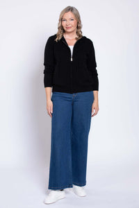 Front view of woman wearing wide leg medium wash jeans, black zip hoodie, and white sneakers