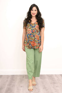Front view of woman standing in floral top and green pants, hands relaxed