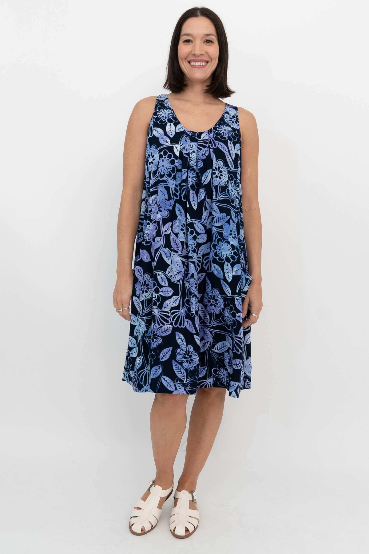 Front view of a woman in a sleeveless, navy blue floral pleated dress with pockets
