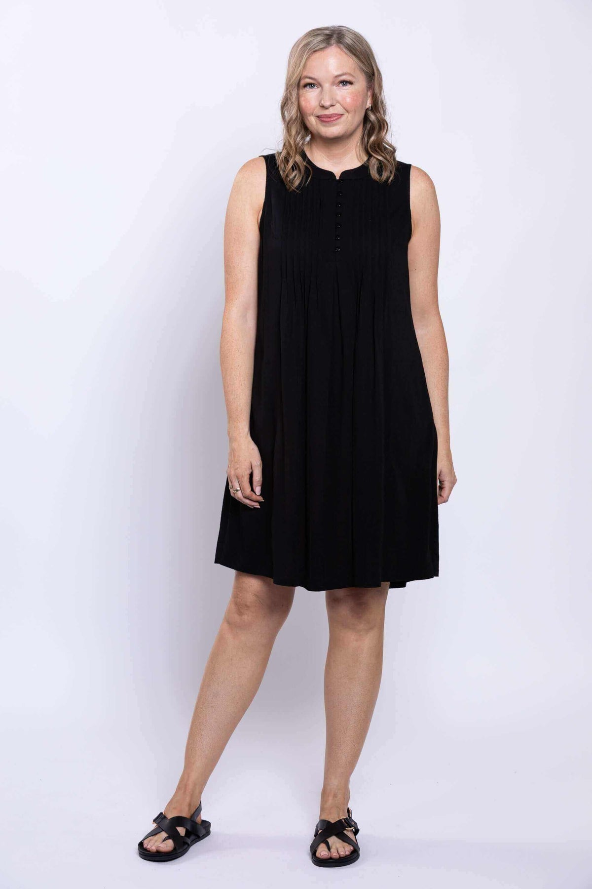 Front view of woman wearing a sleeveless black pintuck A-line dress