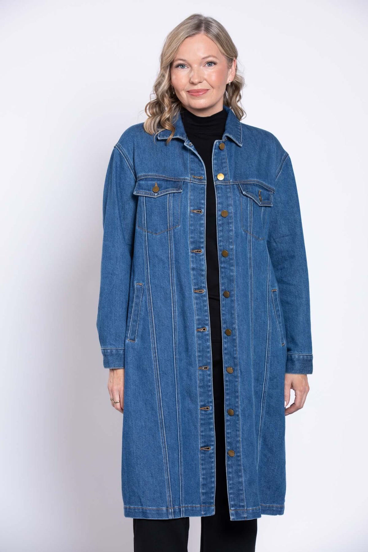 Front view of woman wearing longline denim jacket with button front and flap pockets