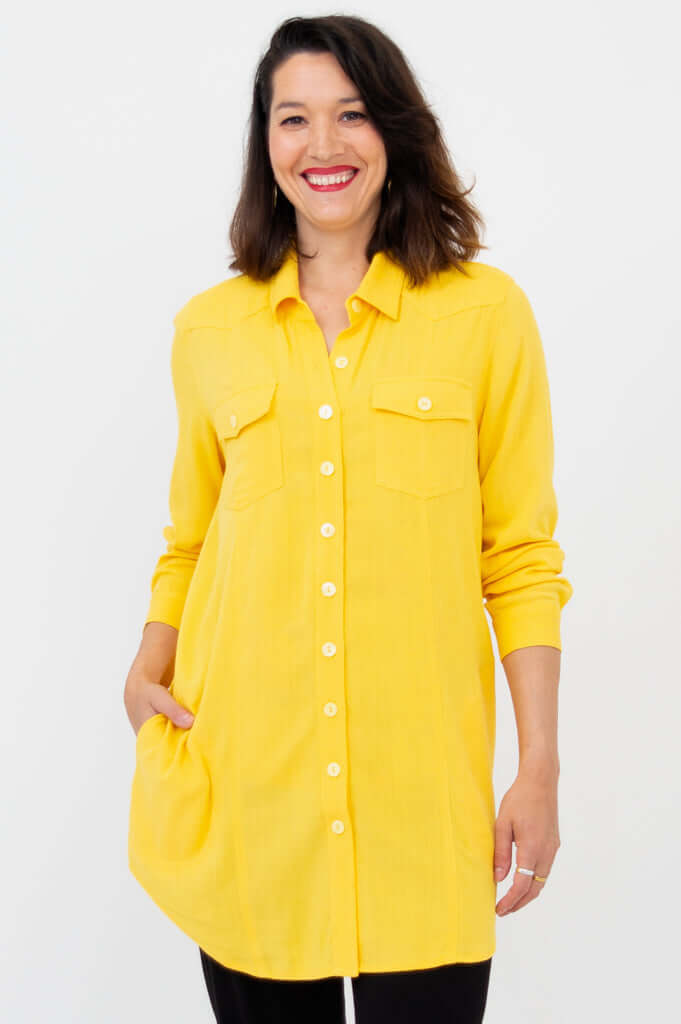 Woman wearing a long yellow button-up shirt tunic with pockets, front view