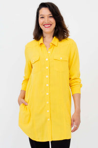 Woman wearing a long yellow button-up shirt tunic with pockets, front view