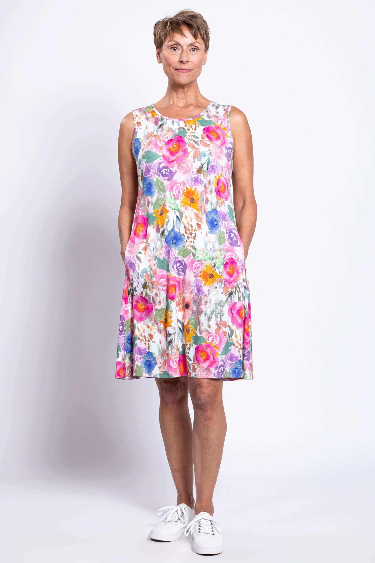 Front view of woman wearing bright floral sleeveless dress with pockets