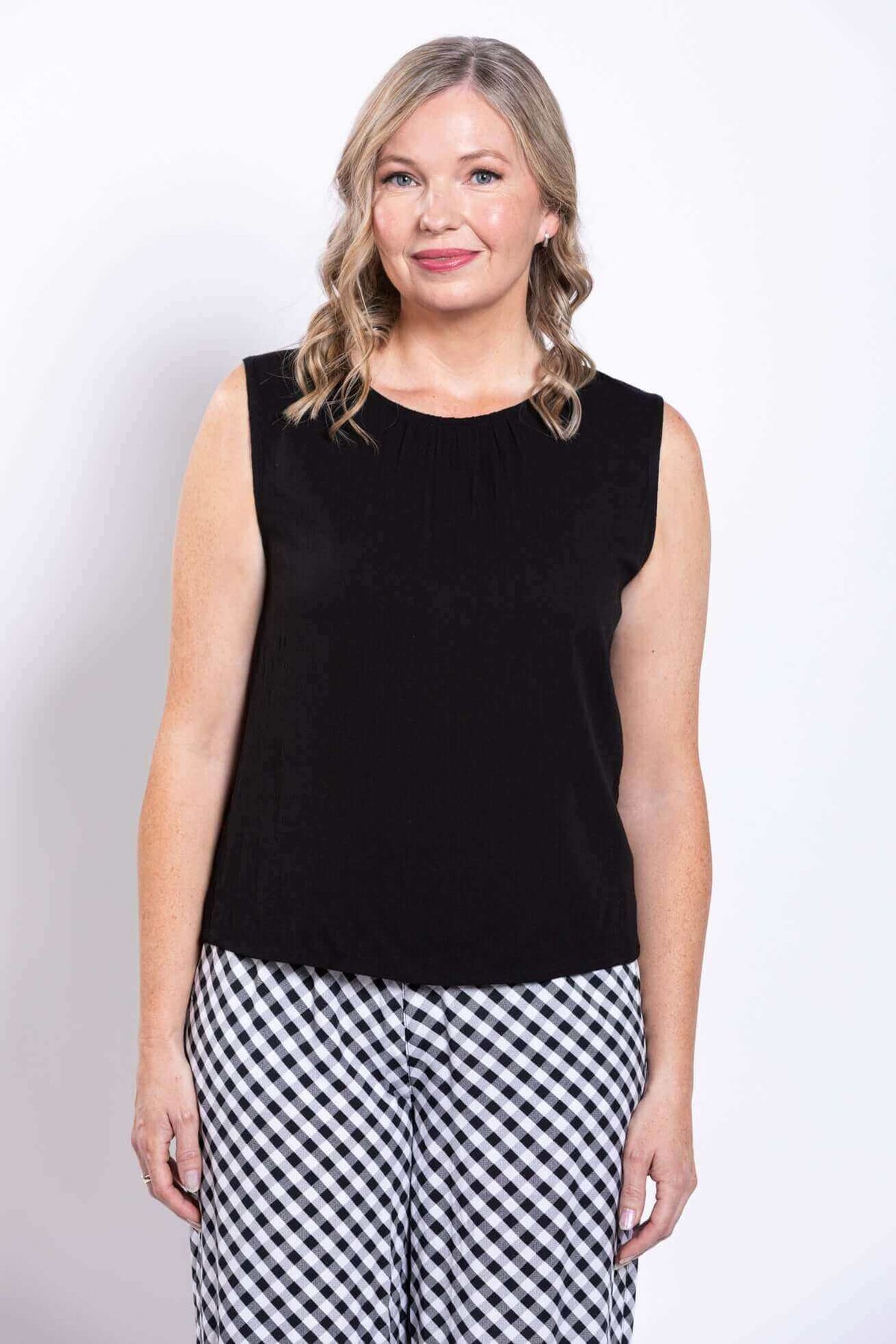 Front view of woman in black sleeveless tank top wth pleated round-neck detail and checkered pants