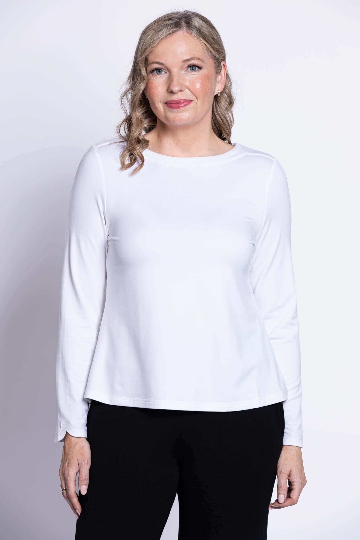 Front view of woman wearing white long sleeve boat neck top with black pants
