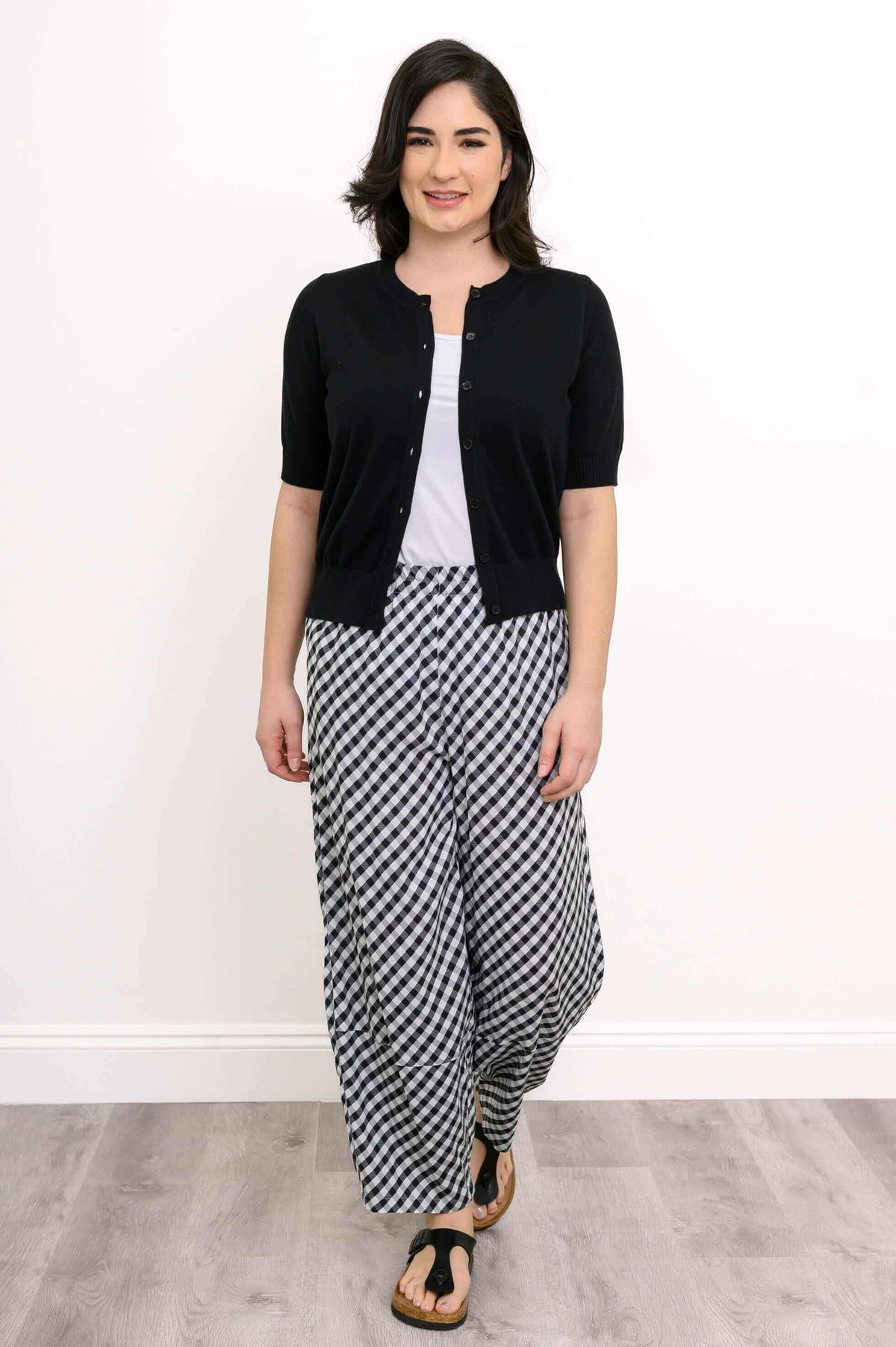 Front view of woman walking in black and white gingham pants and black cardigan