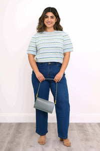 Full-body view of woman in blue eyelet stripe short sleeve sweater, jeans, and heels holding a gray bag