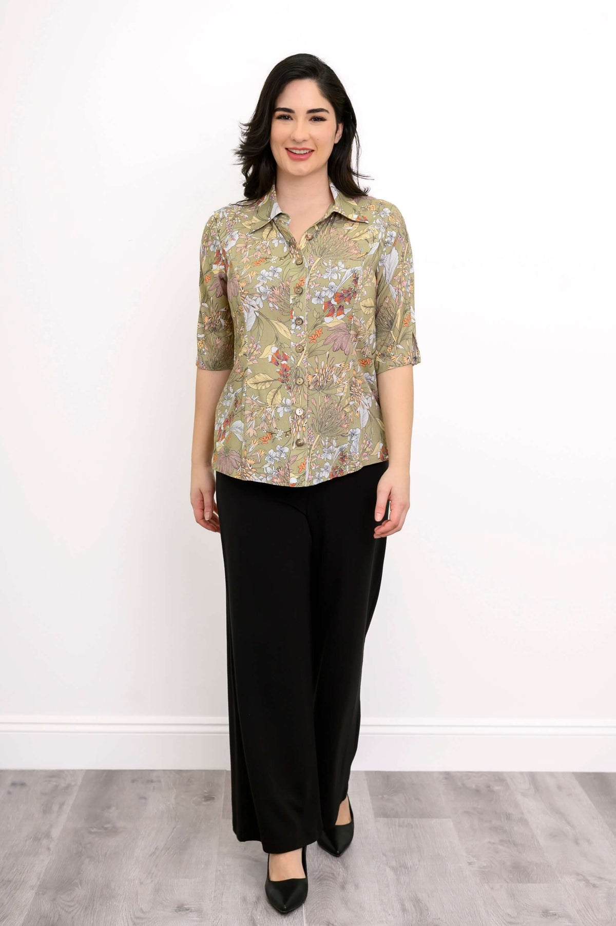 Full-body front view of woman modeling a button-up floral blouse and black pants