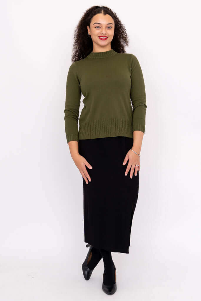 Full-body view of a woman in an olive green sweater and black skirt