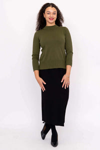 Full-body view of a woman in an olive green sweater and black skirt
