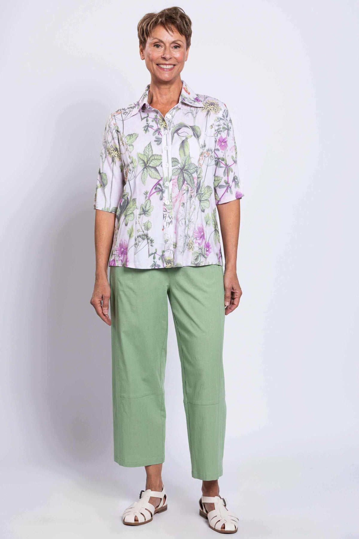 Full-body front view of a woman in a floral blouse and light green pants with white sandals