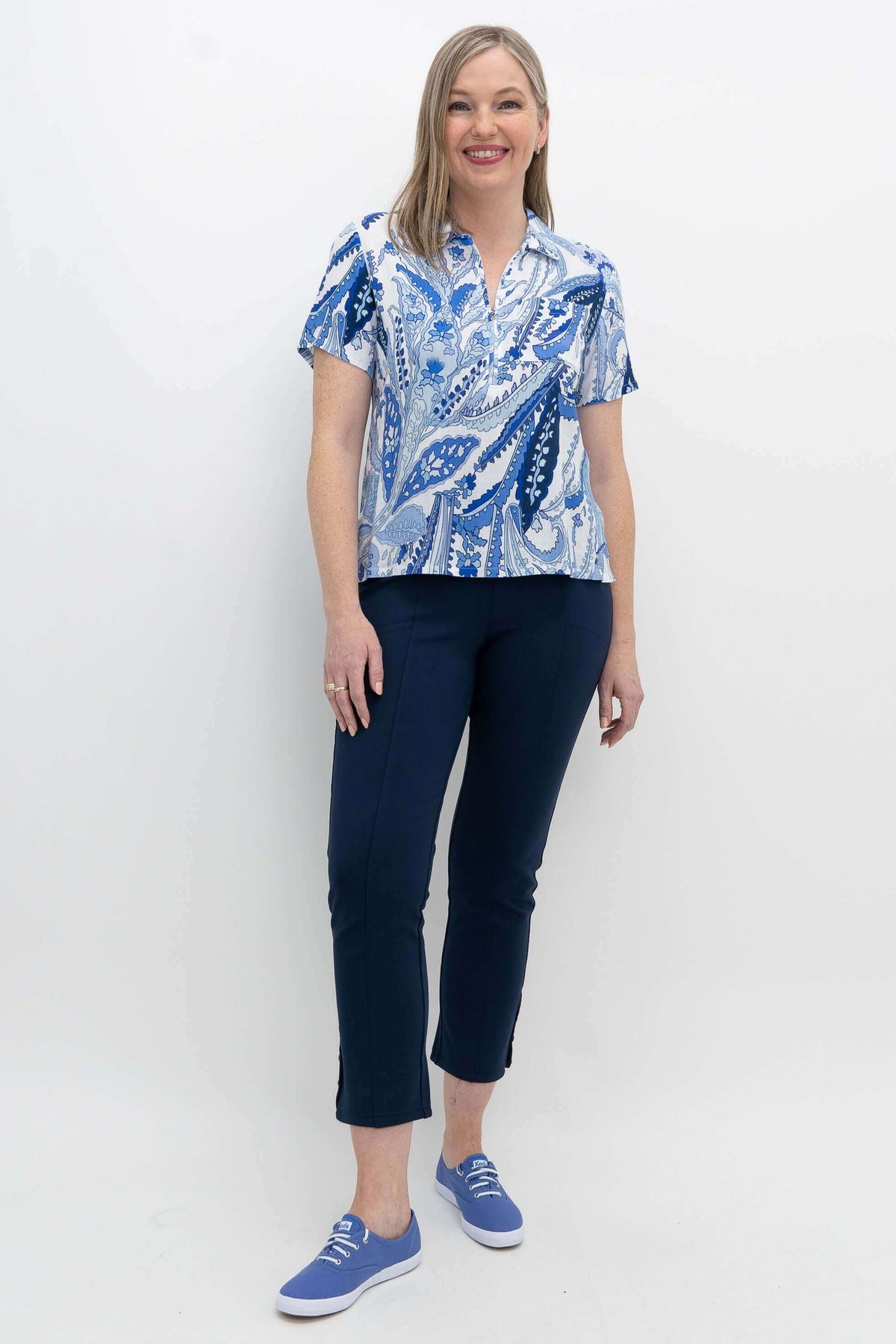 Full-body shot of a woman in a blue paisley Lala top paired with dark trousers and sneakers