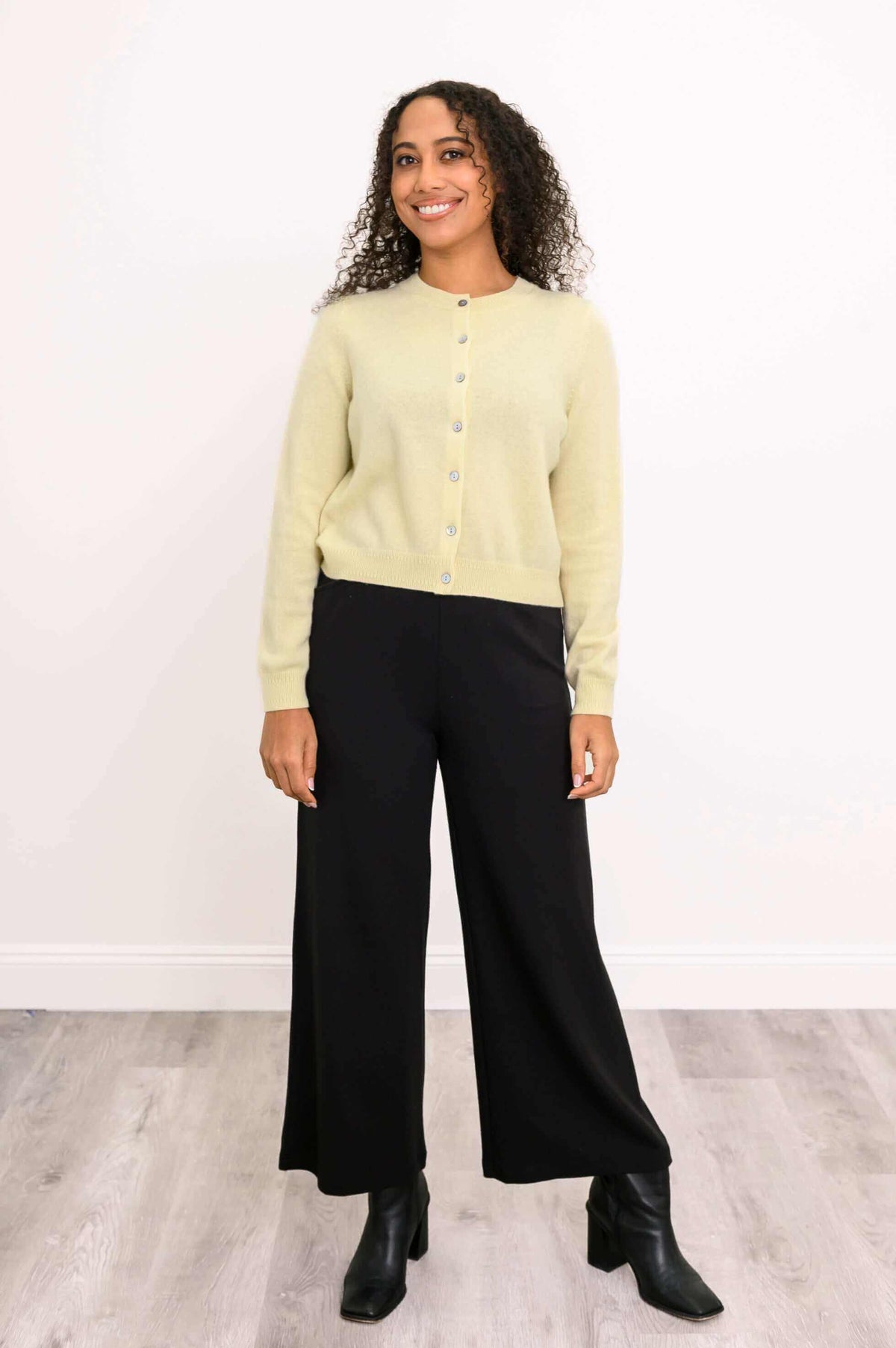 Full-body view of a woman in a light yellow buttoned cardigan and black wide-leg pants