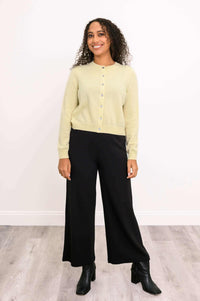Full-body view of a woman in a light yellow buttoned cardigan and black wide-leg pants
