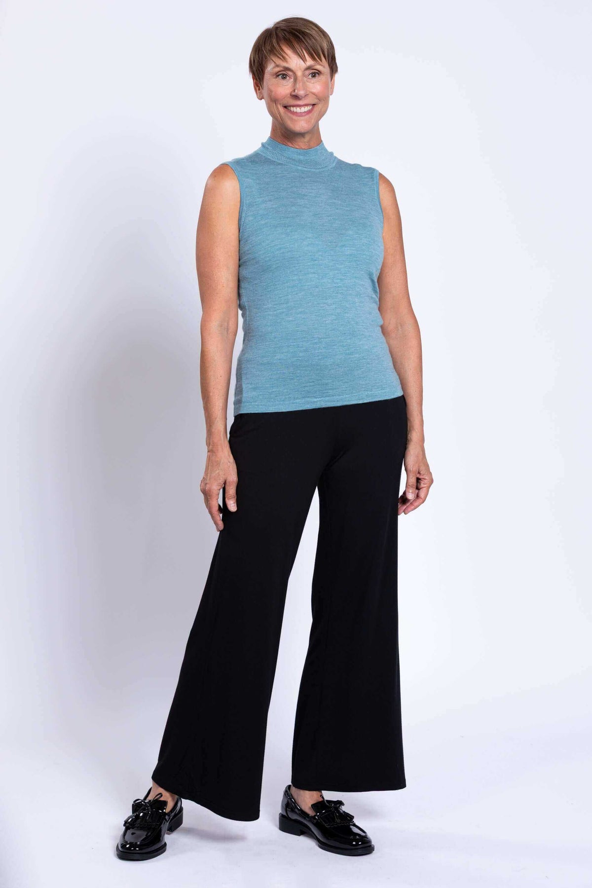 Full-body view of a woman in a sleeveless blue merino sweater and black wide-leg pants