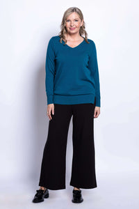 Full view of woman in teal v-neck sweater and black wide-leg pants