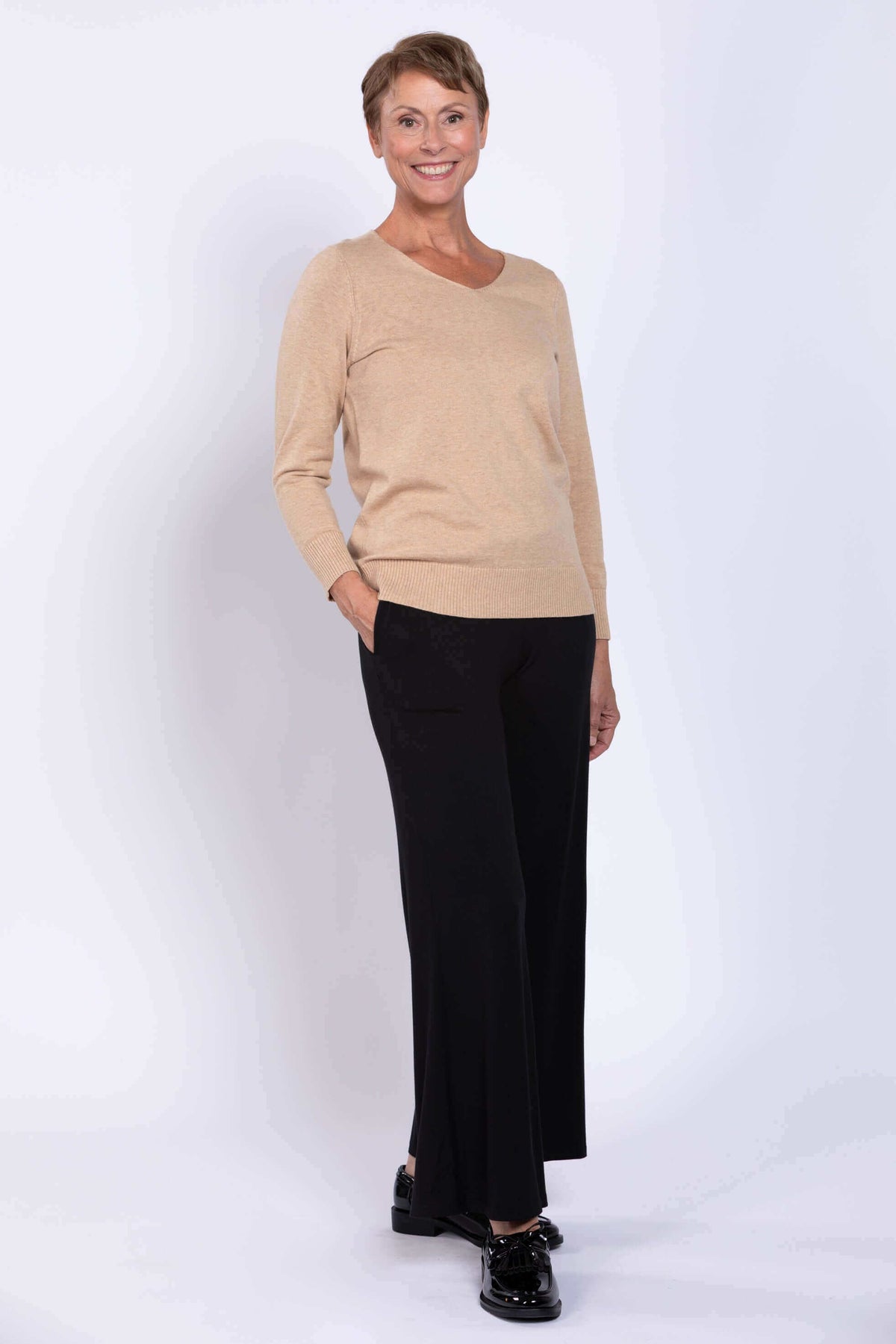 Full-body view of woman in beige V-neck sweater and black wide-leg pants