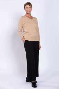 Full-body view of woman in beige V-neck sweater and black wide-leg pants
